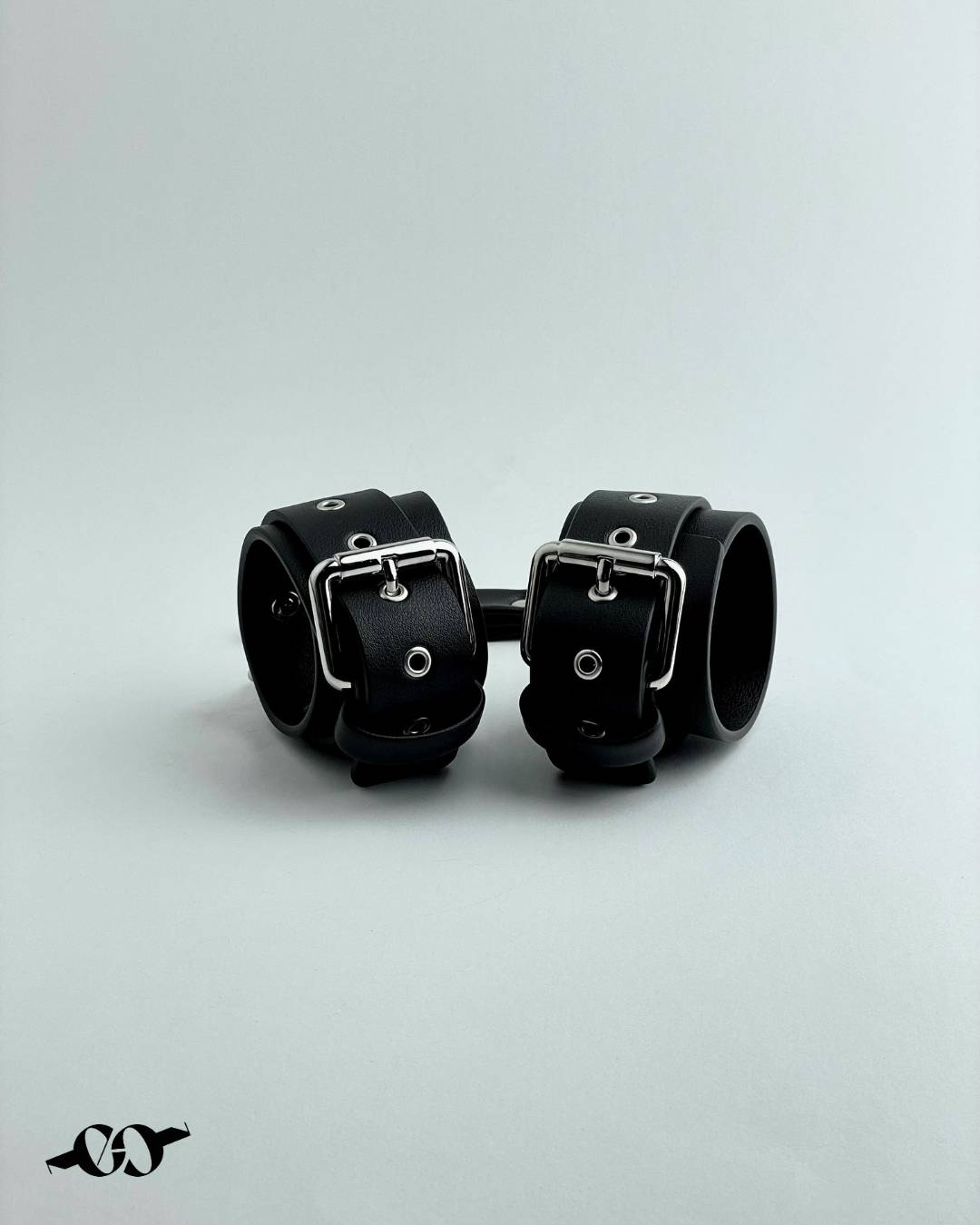 A pair of black leather cuffs, secured with metal buckles, displayed against a white background.