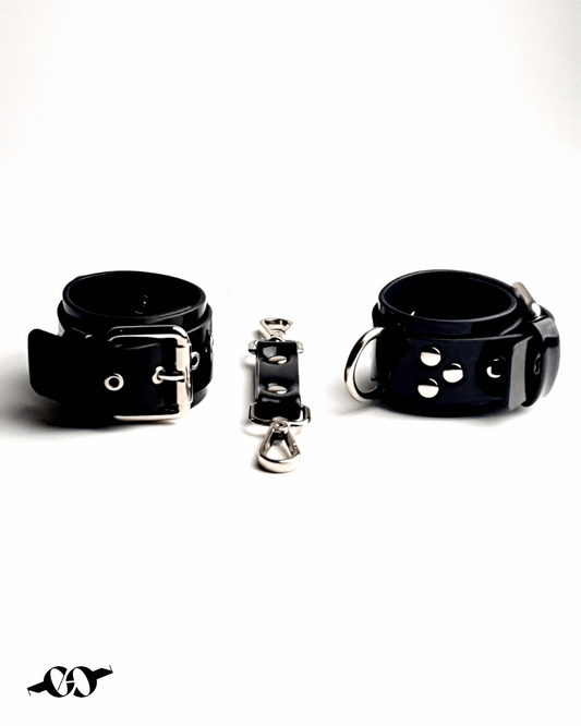 A black patent leather handcuff bracelet with adjustable straps and a central fastener, displayed on a white background.