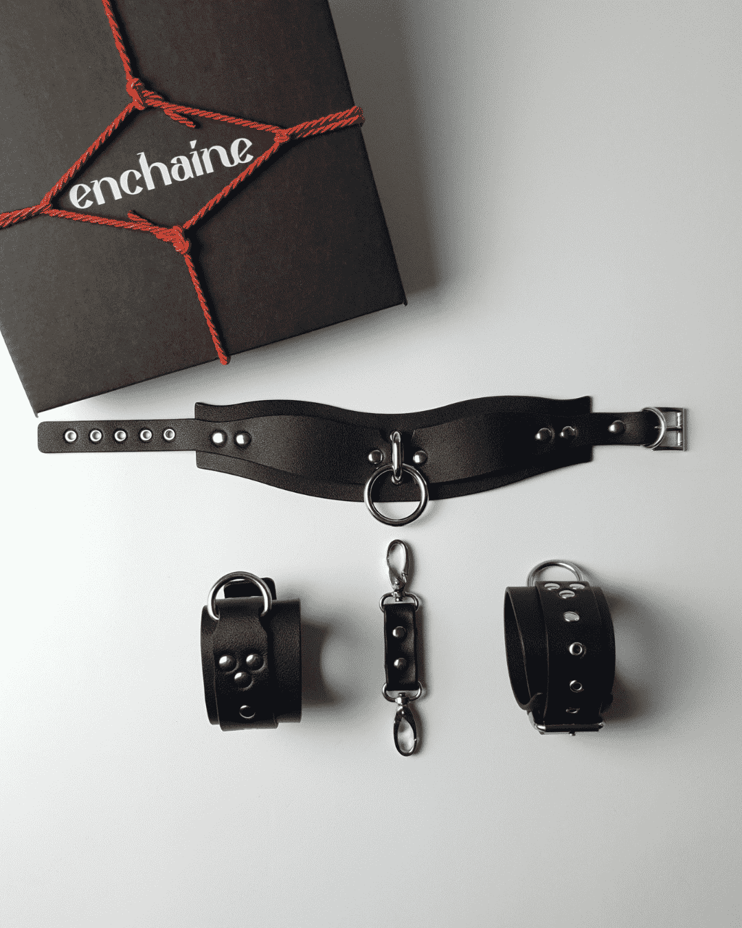 A black BDSM starter kit by ENCHAINE, including a choker and handcuffs, displayed next to its packaging.