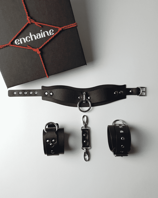 A black BDSM starter kit by ENCHAINE, including a choker and handcuffs, displayed next to its packaging.