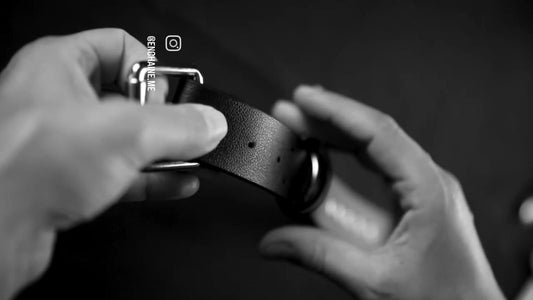 Hands fastening a black vegan leather collar with silver buckle and O-ring, close-up
