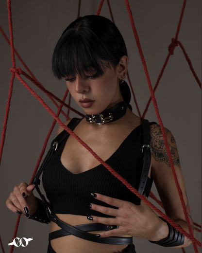 A person wearing a black harness belt, standing in a room with a web-like structure made of red ropes.
