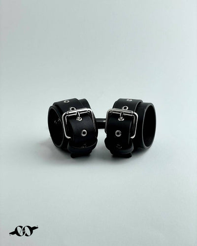 A pair of black leather cuffs, secured with metal buckles, displayed against a white background.