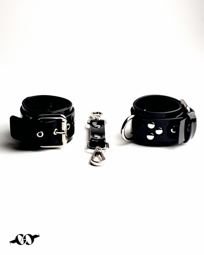 A black patent leather handcuff bracelet with adjustable straps and a central fastener, displayed on a white background.